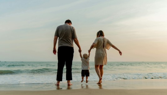 Parents hold their young child's hands on a beach. When your child triggers overwhelming anxiety, can you still be present? Anxiety therapy in Delray Beach, FL, helps parents manage their emotional responses while staying connected.