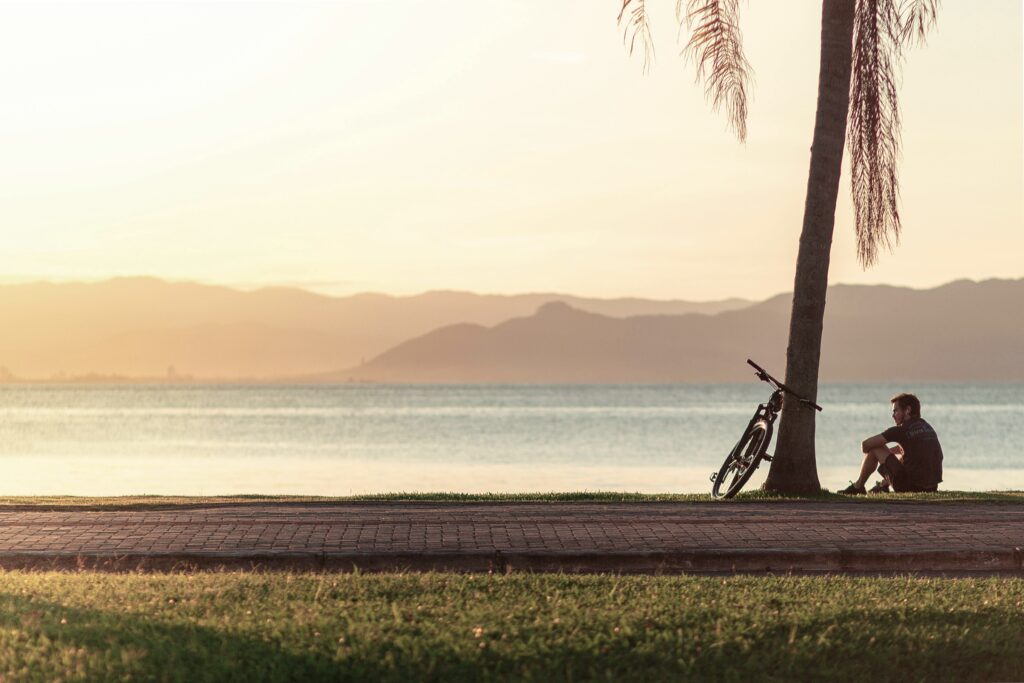 A man sitting alone on a beach near a palm tree. Overthinking causes anxiety, and sometimes anxiety causes overthinking. Therapy for anxiety in Delray Beach, FL, can help you end this cycle and work toward newfound peace.