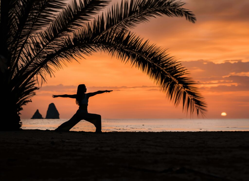 A woman's silhouette holds a warrior yoga pose beneath a palm tree at sunset. Coping strategies like mindfulness and movement can help break the cycle of overthinking. Anxiety therapy in Delray Beach, FL, can guide you toward lasting calm and resilience.